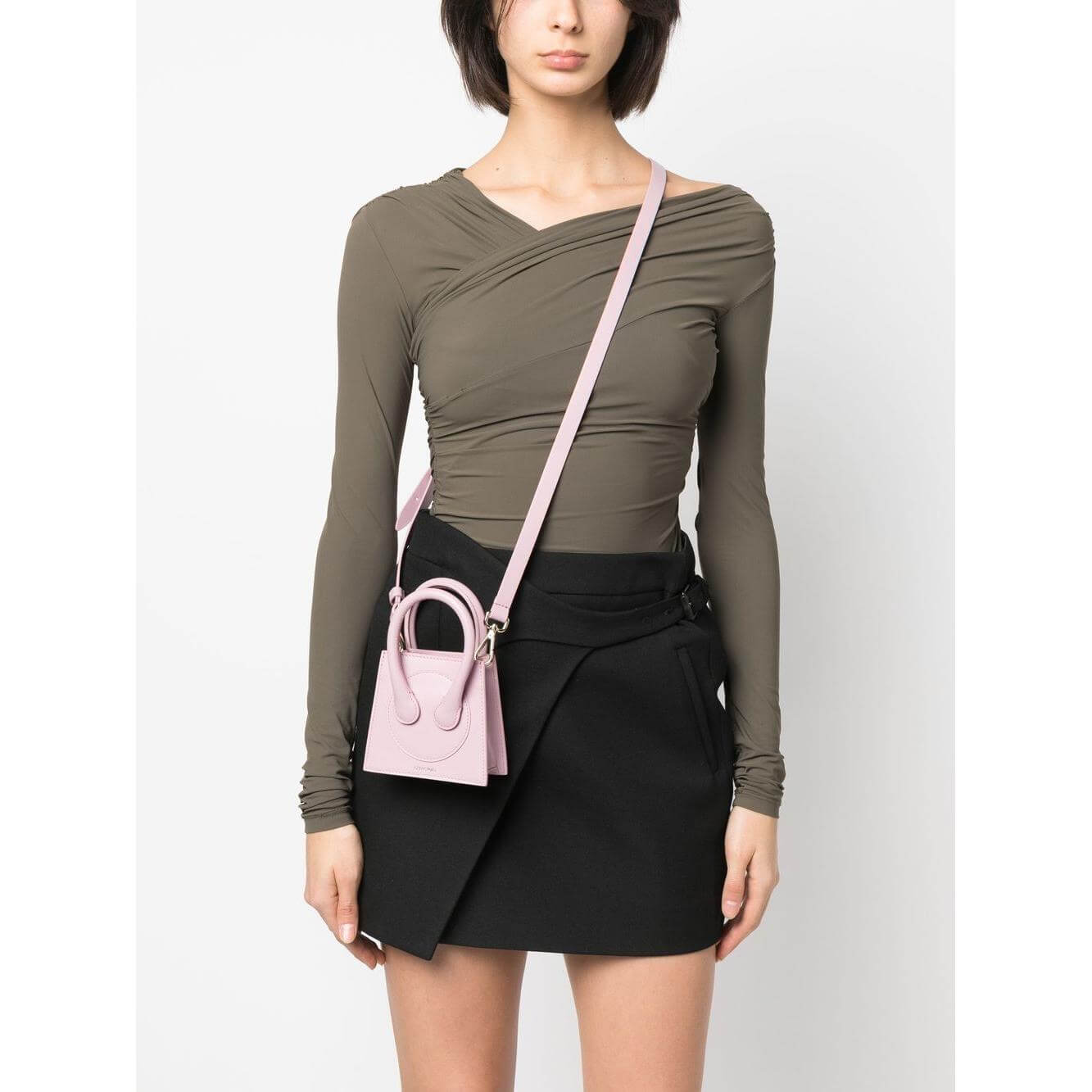 Model wearing Az Factory x Ester Manas Cake mini tote bag in light pink leather with a crossbody strap, styled with olive top and black skirt.
