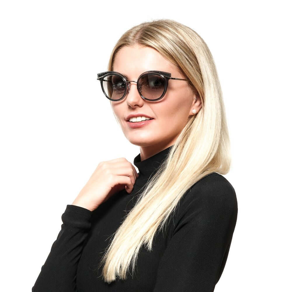 Woman wearing Swarovski gray oval sunglasses with mirrored lenses and metal frame, 100% UVA & UVB protection, sleek and stylish design.