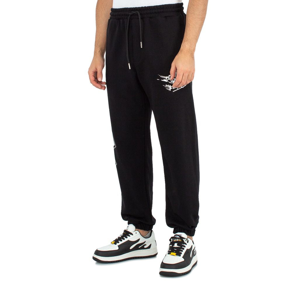 Comme Des Fuckdown black cotton men's sweatpants with bold logo prints, model standing, paired with trendy sneakers.