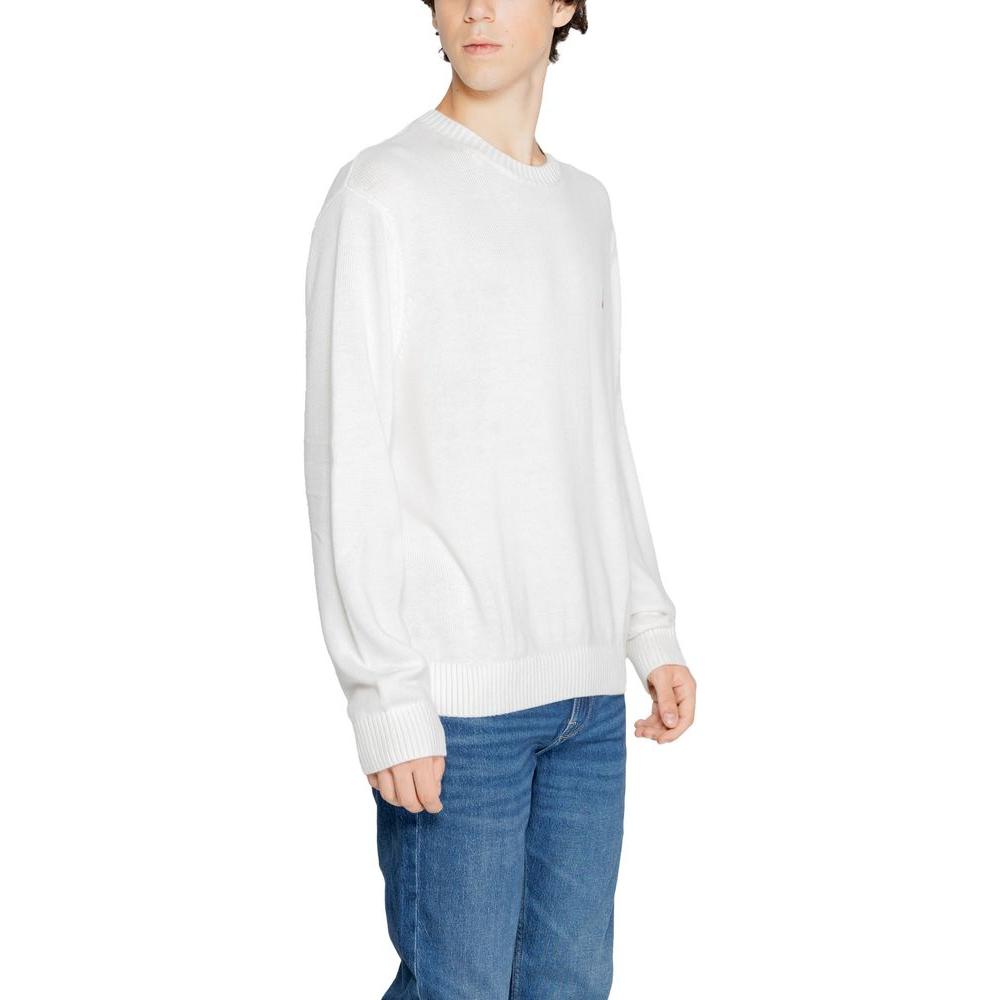 Man wearing Tommy Hilfiger white recycled polyester sweater, fall/winter collection, showcasing sustainable men's knitwear fashion.