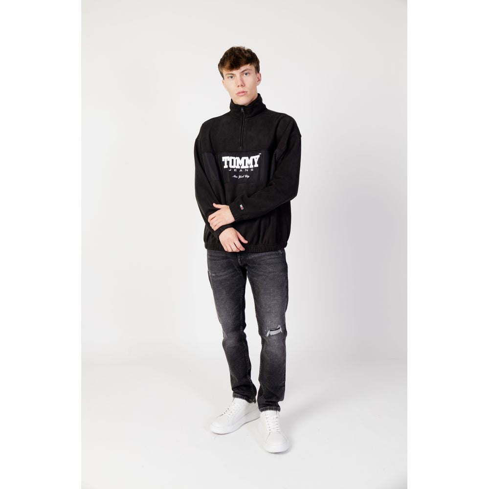 Alt Tag: Men's black Tommy Hilfiger recycled polyester sweater, fall/winter collection, modeled with jeans and white sneakers.