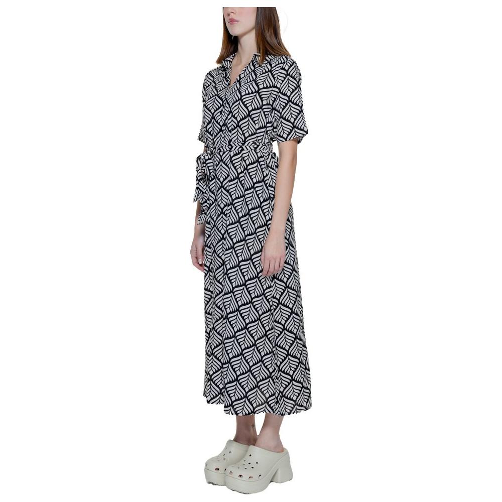 Side view of a long geometric patterned dress with short sleeves and tie waist, worn by a model with white platform shoes.
