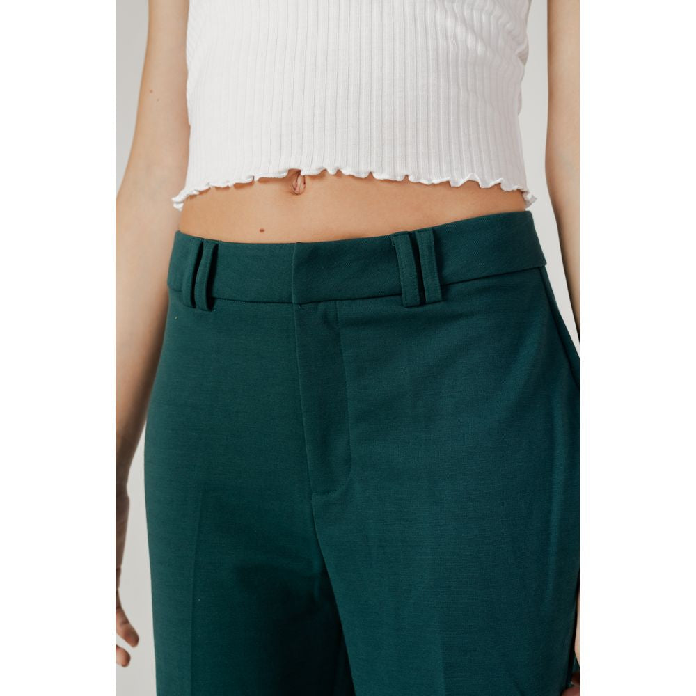 Woman wearing green polyester cigarette pants, fall/winter collection, showcasing front design detail.