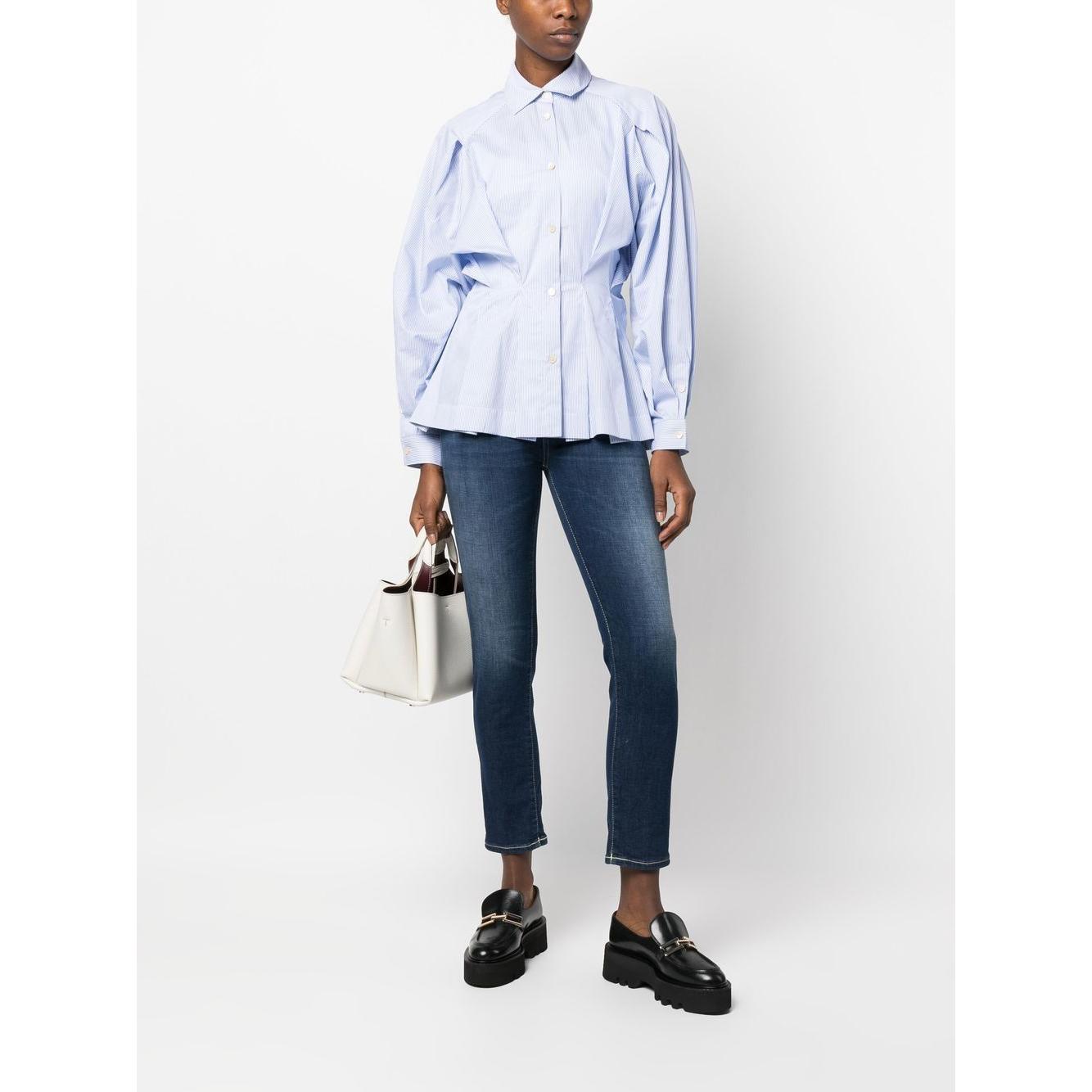 Model wearing pastel blue gathered-waist cotton shirt by Palmer Harding, paired with dark jeans and black shoes, holding a white handbag.