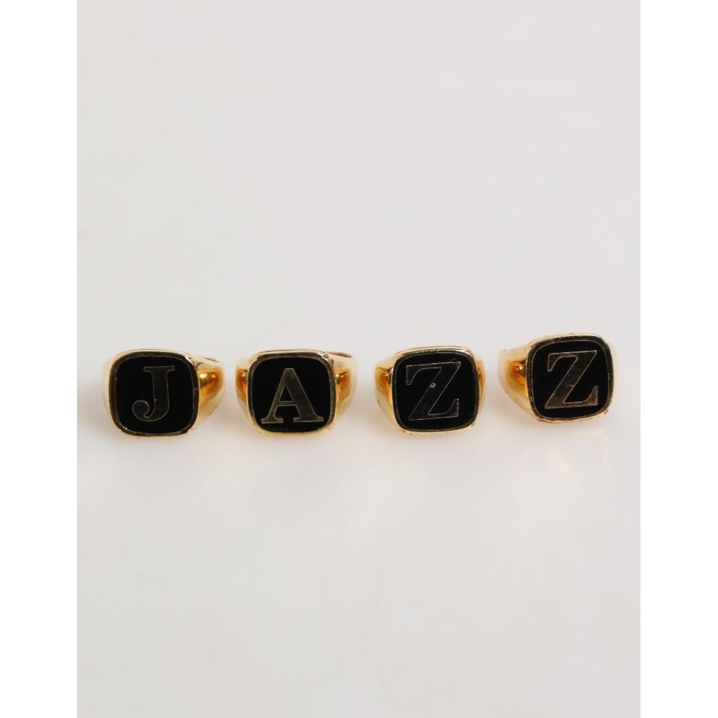 Dolce & Gabbana Gold Tone Brass JAZZ Letter Set 4 Pieces Adjustable Ring, featuring bold black letters on elegant gold-tone rings.