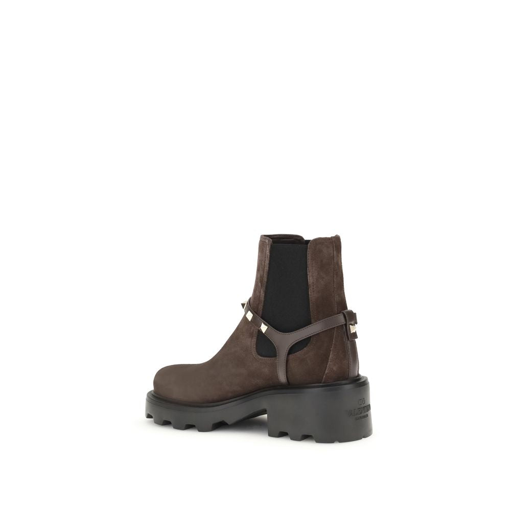 Valentino Garavani Brown Calf Leather Bos Taurus Chelsea Boots with lug sole and "V" buckle on white background.