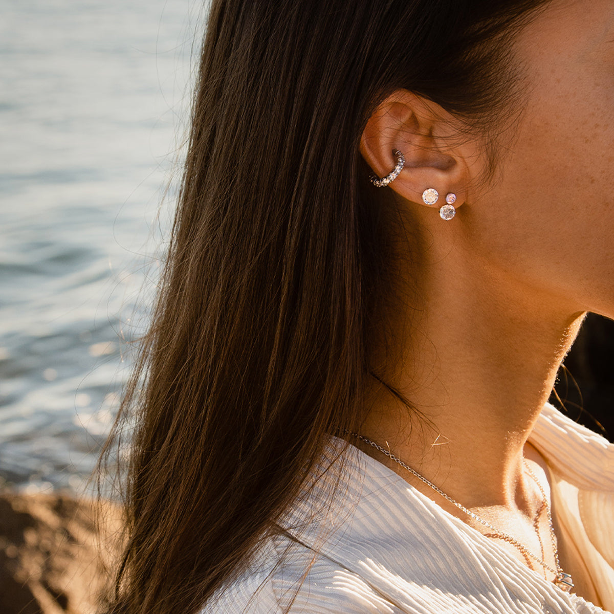 Woman wearing AN JEWELS JEWELRY Mod. AL.NLFY01 earrings by the seaside, showcasing elegant style and craftsmanship.