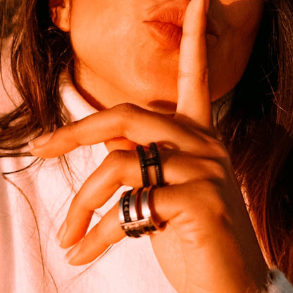 Close-up of woman wearing AN JEWELS JEWELRY Mod. AR.R2NS02BK-8 ring, gesturing silence with finger on lips in warm sunlight