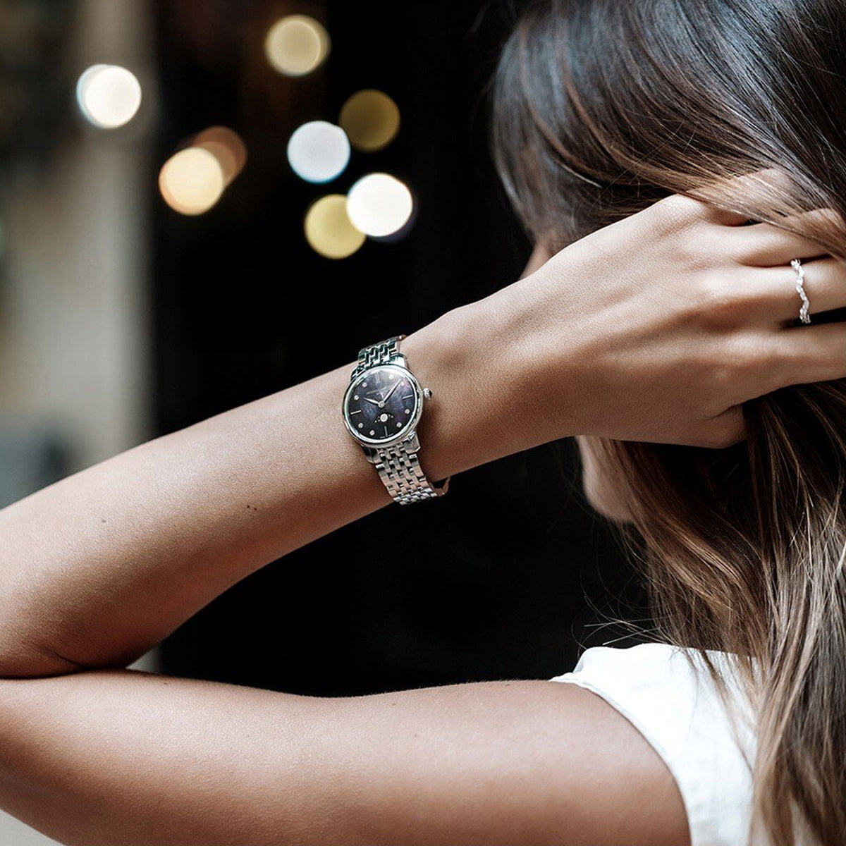Woman wearing a FREDERIQUE CONSTANT MOD. FC-206MPBD1S6B watch with a stylish silver bracelet, featured in a chic and elegant setting.