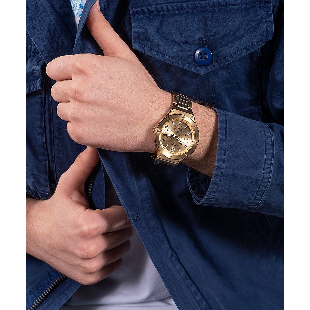 Gent wearing GUESS Mod. GW0454G2 quartz analog watch with a gold dial and silver band, 44mm case, water resistant to 5 ATM