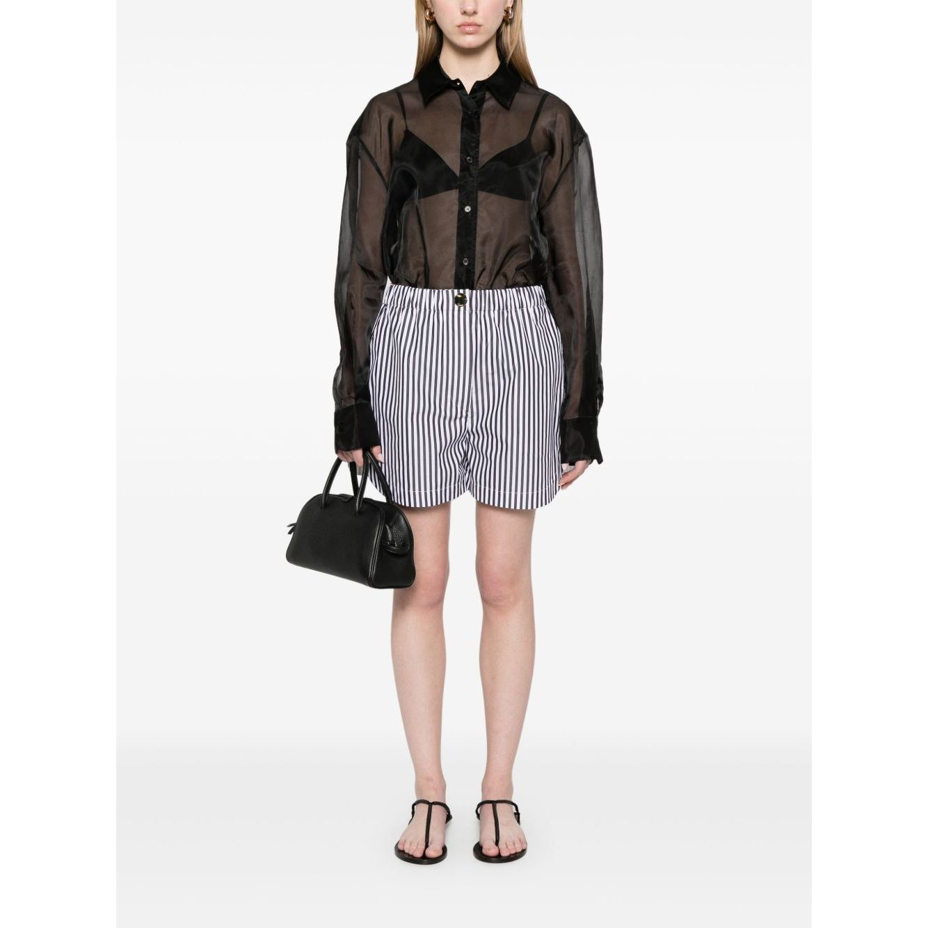 Woman wearing SportMax black striped shorts with elastic waistband, front button, and zip fastening, paired with a sheer black shirt.