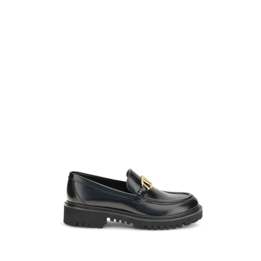 Valentino Garavani Black Leather Slip-On Loafers with brass VLogo detail on a rubber lug sole, side view.
