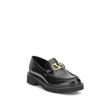 Valentino Garavani Black Leather Slip-On Loafers with brass VLogo and rubber lug sole, showcasing classic and contemporary style.